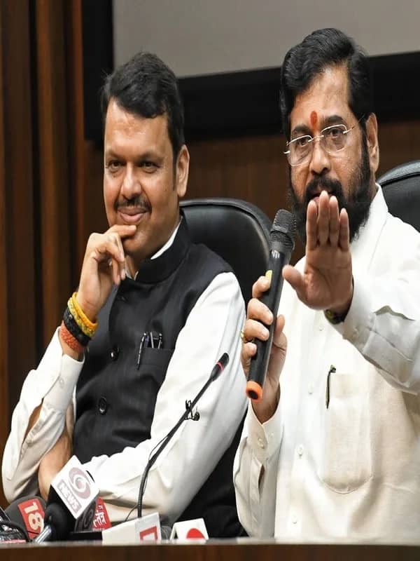 दो आदमी प्रेस कॉन्फ्रेंस में बैठे हैं, एक बोल रहा है और दूसरा सुन रहा है।