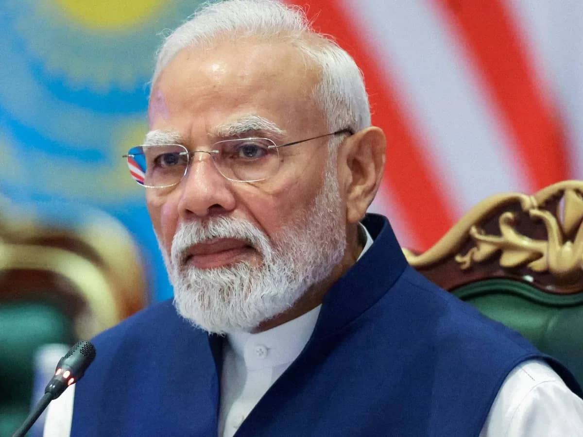 एक व्यक्ति चश्मा पहने हुए, दाढ़ी और मूंछ के साथ, नीले रंग की जैकेट पहने हुए।